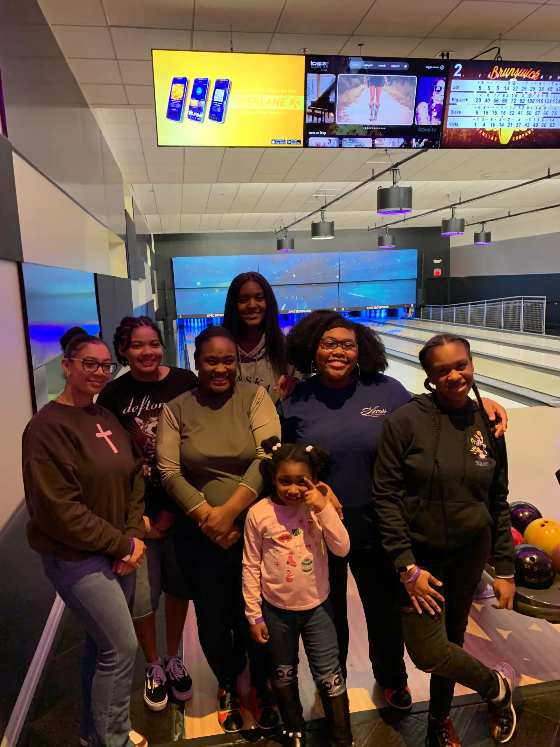 Young women and a child smiling together at an autism-friendly bowling outing